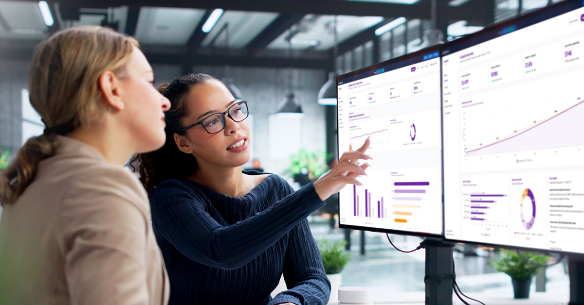 Two employees looking at a data migration dashboard on computer screens.