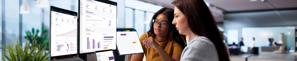 Two employees looking at data dashboards on computer screens.