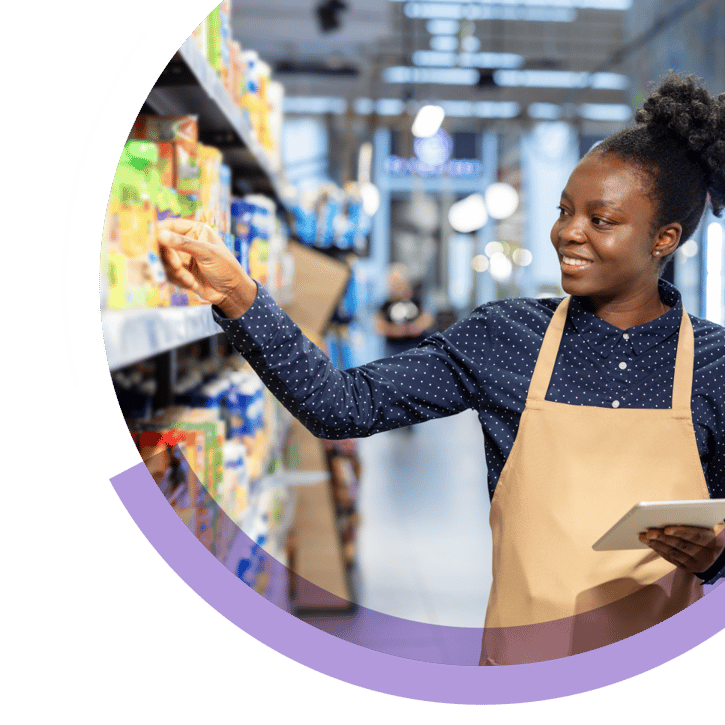 Store employee restocking packaged goods on a supermarket shelf while holding a tablet.