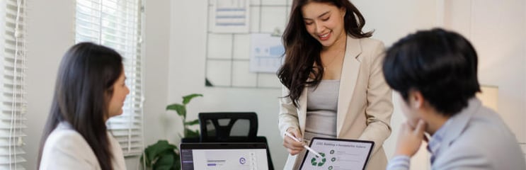 Consultant presenting sustainability metrics on a tablet during a meeting, showing ESG indicators and circular economy graphics used for sustainability reporting and strategy discussions.