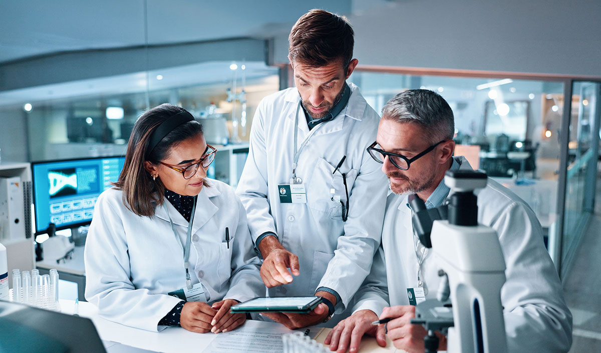Three pharma employees in lab coats looking at a tablet.