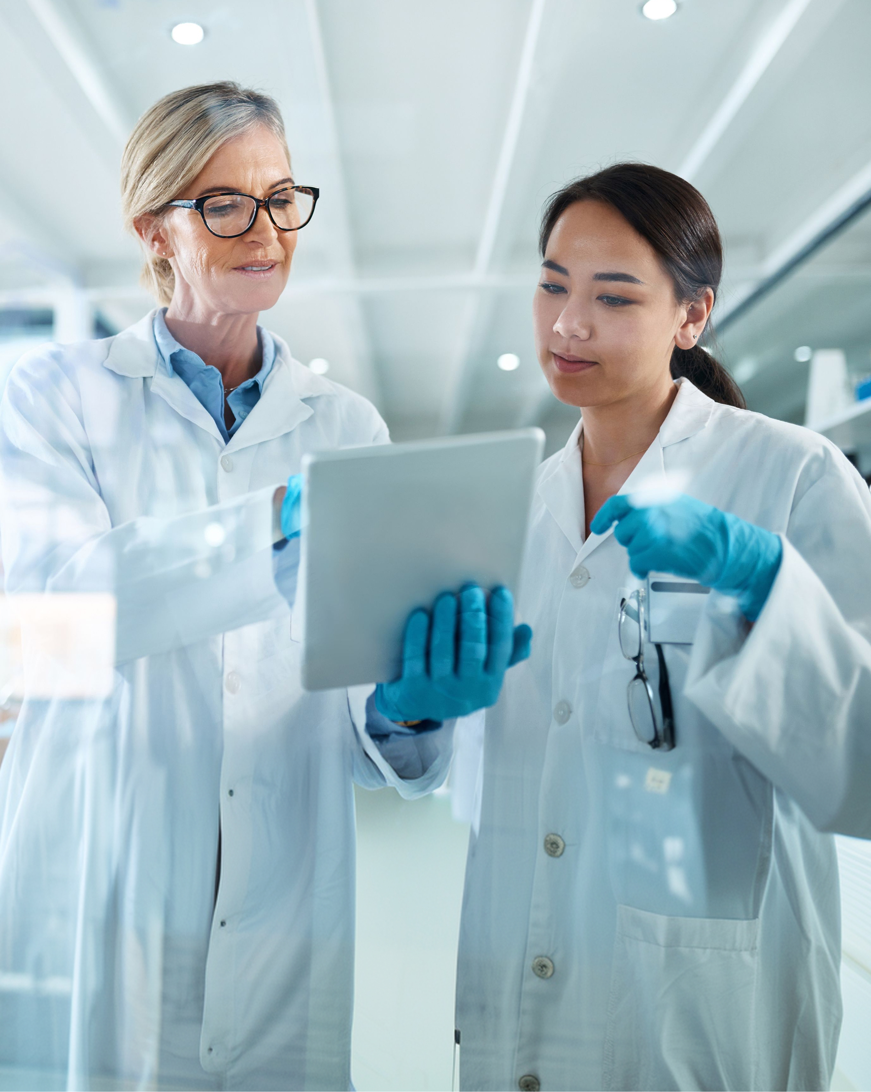 Two female pharma employees wearing lab coats looking at a tablet.