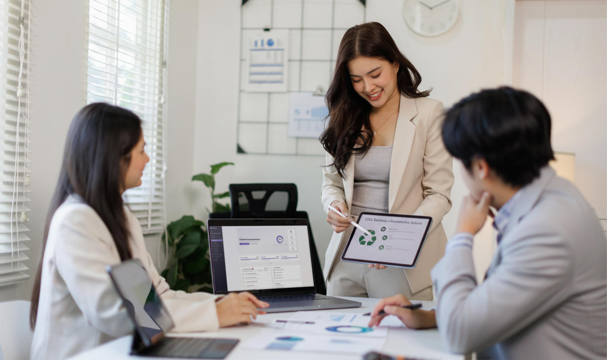 Business professional presenting sustainability data on a tablet, with a laptop displaying the Sustainability Reporting Hub dashboard in a meeting setting